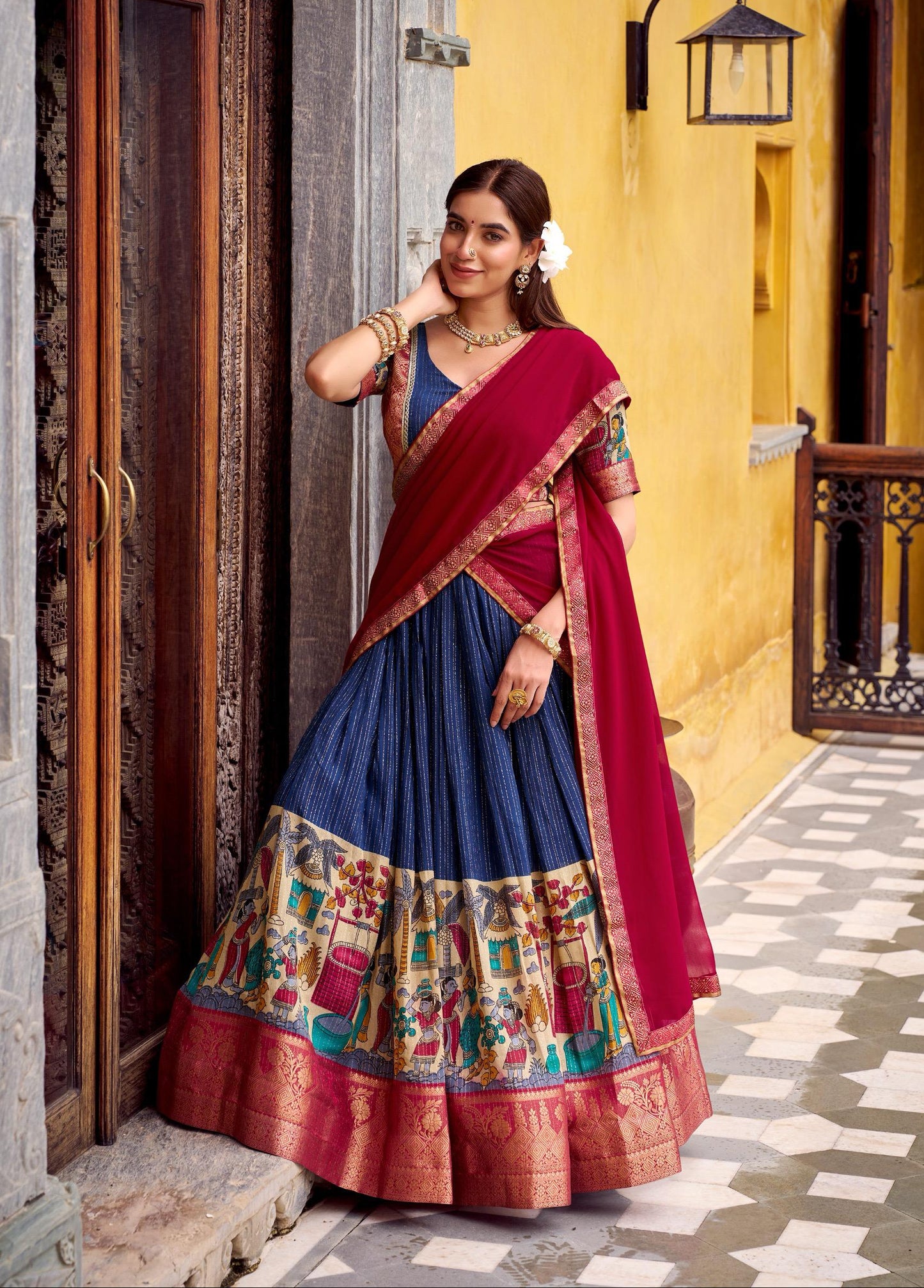 Woman in a traditional multicolored saree standing in front of a yellow wall.
