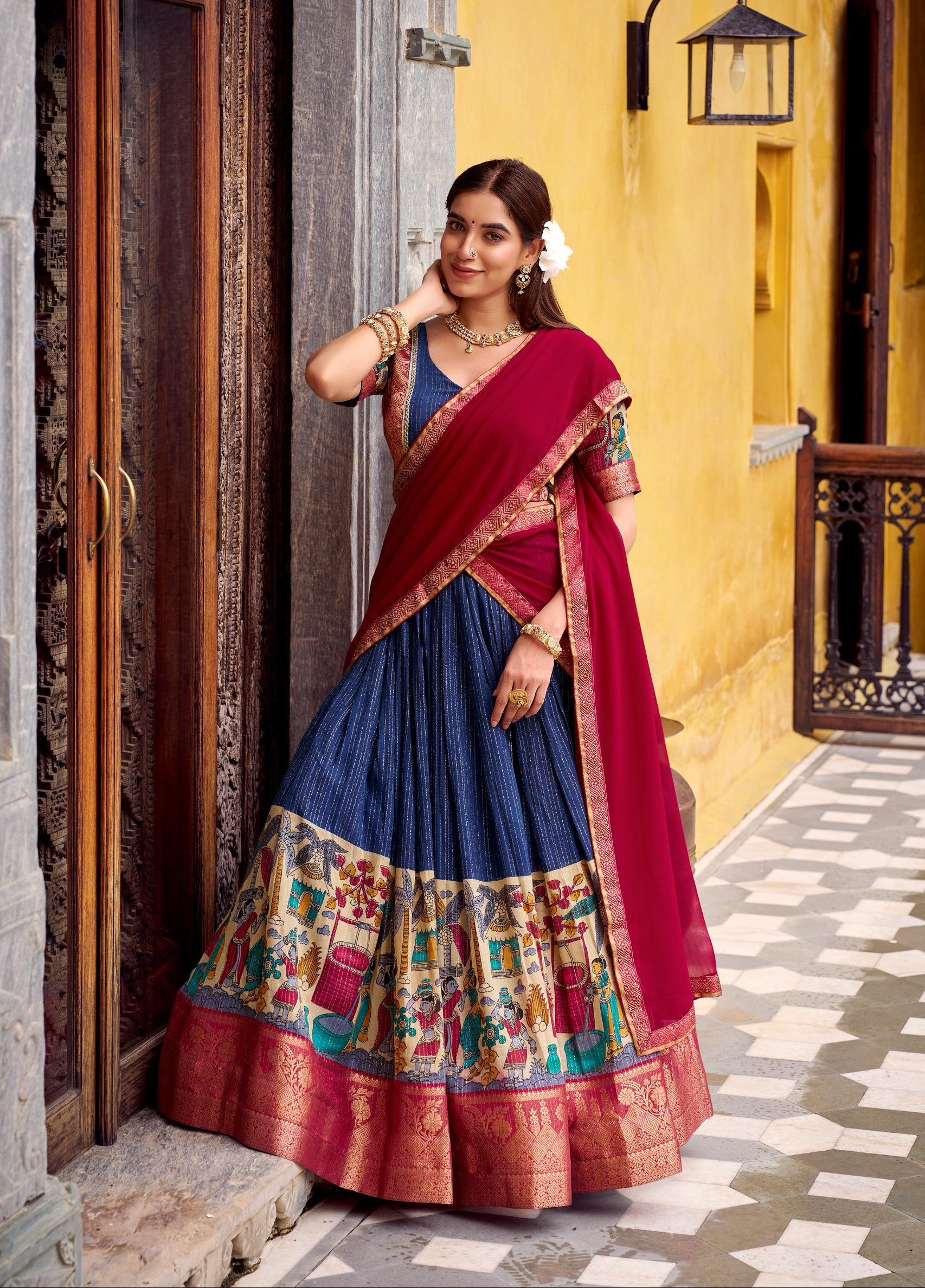 Woman in a traditional multicolored saree standing in front of a yellow wall.