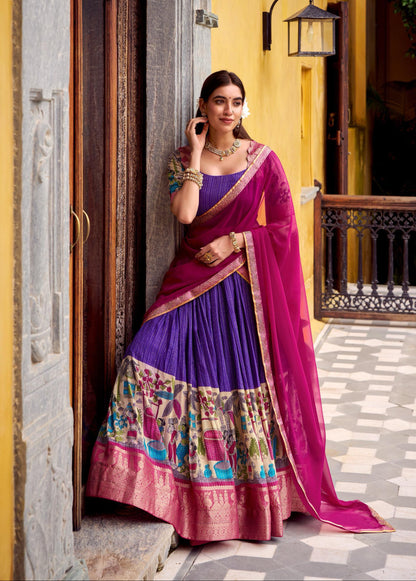 Woman in a traditional purple and pink saree standing in front of a yellow wall.