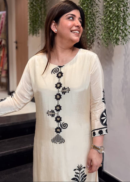 Woman wearing a cream-colored kurta with black floral embroidery indoors.