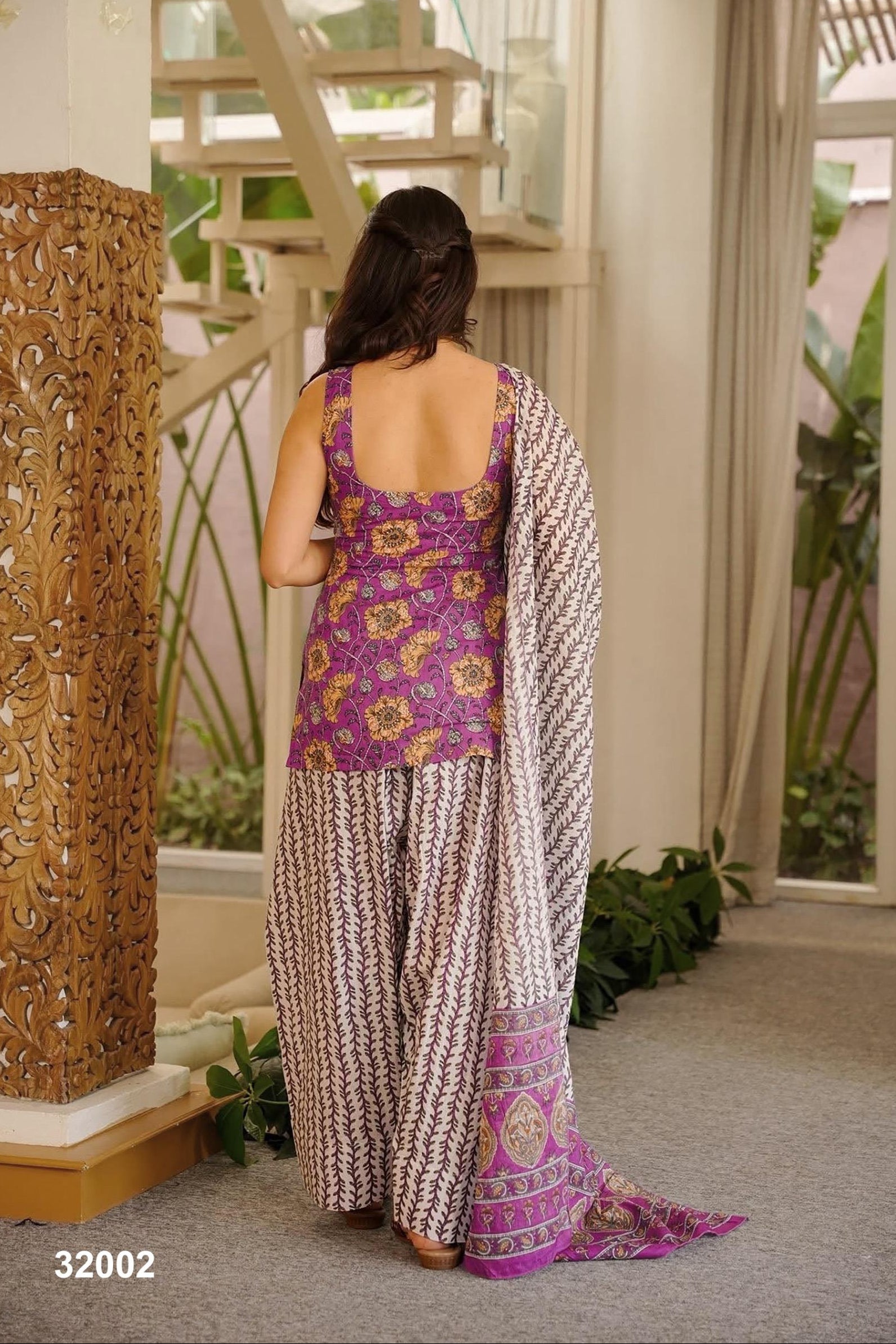 Woman in a patterned outfit standing in a room with decorative elements.