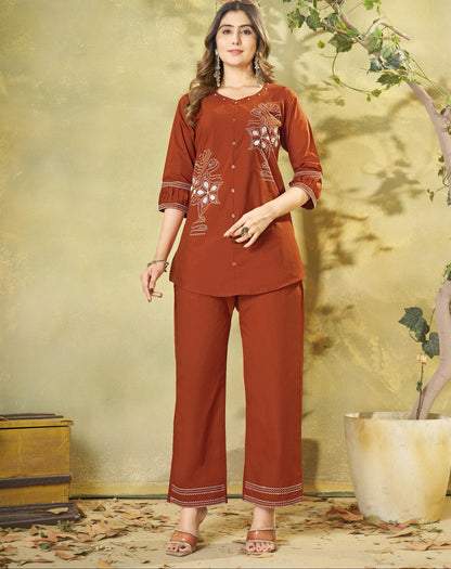 Woman wearing a rust-colored traditional outfit with floral patterns in an indoor setting.