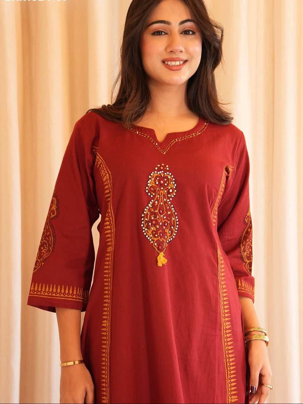 Woman wearing a red embroidered dress against a beige curtain background