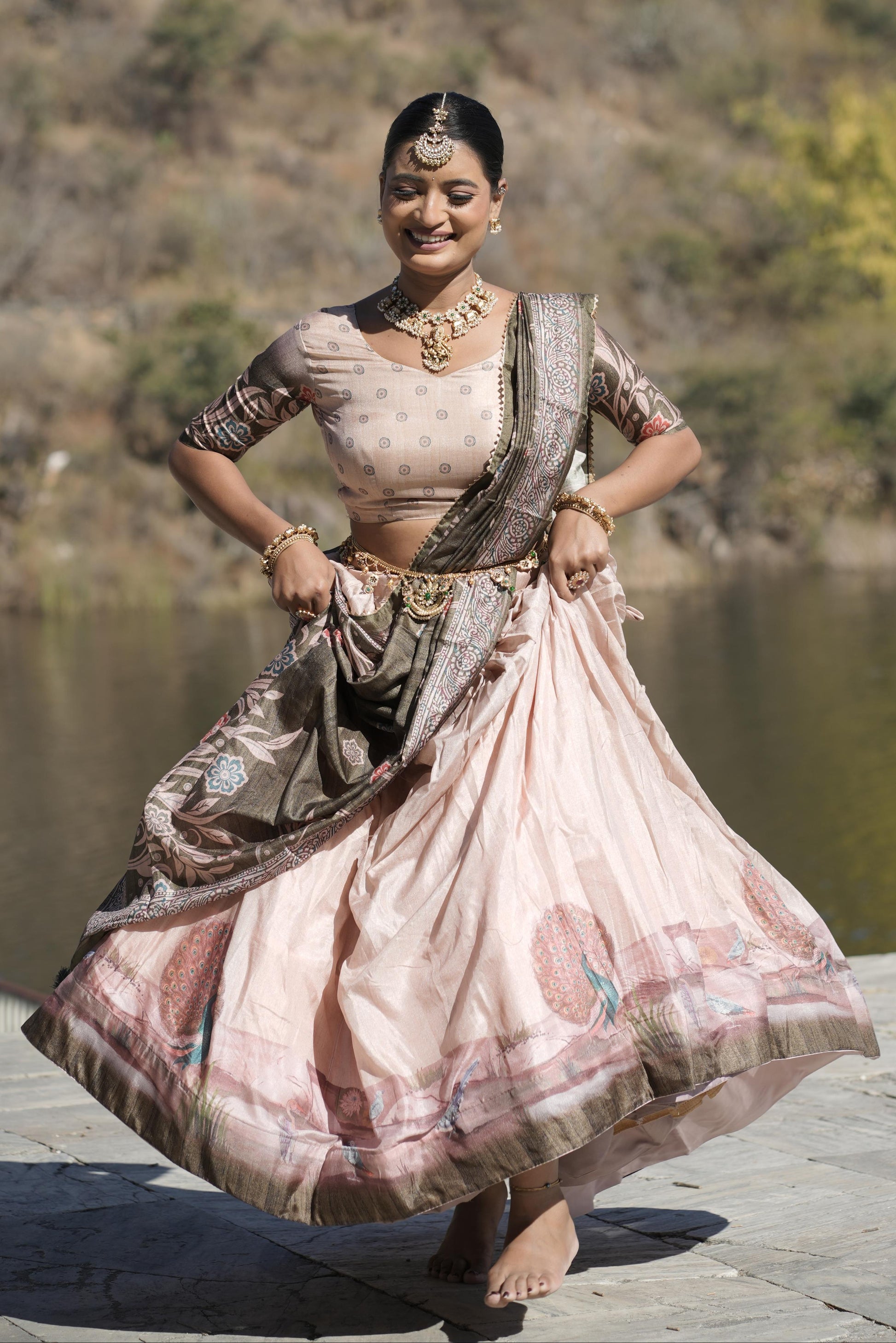 Woman in traditional attire standing by a lake with mountains in the background