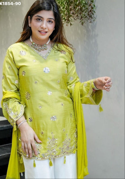 Woman wearing a light green embroidered traditional outfit with white pants, standing against a neutral background.