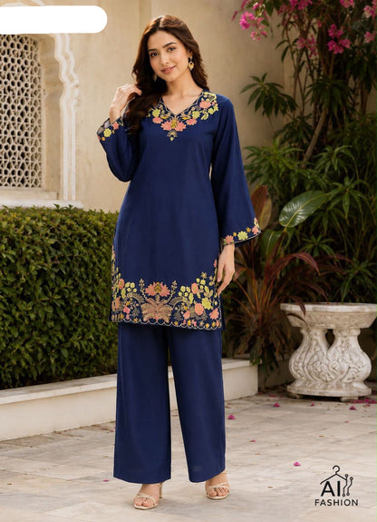 Woman wearing a blue embroidered outfit standing outdoors with plants and a building in the background.