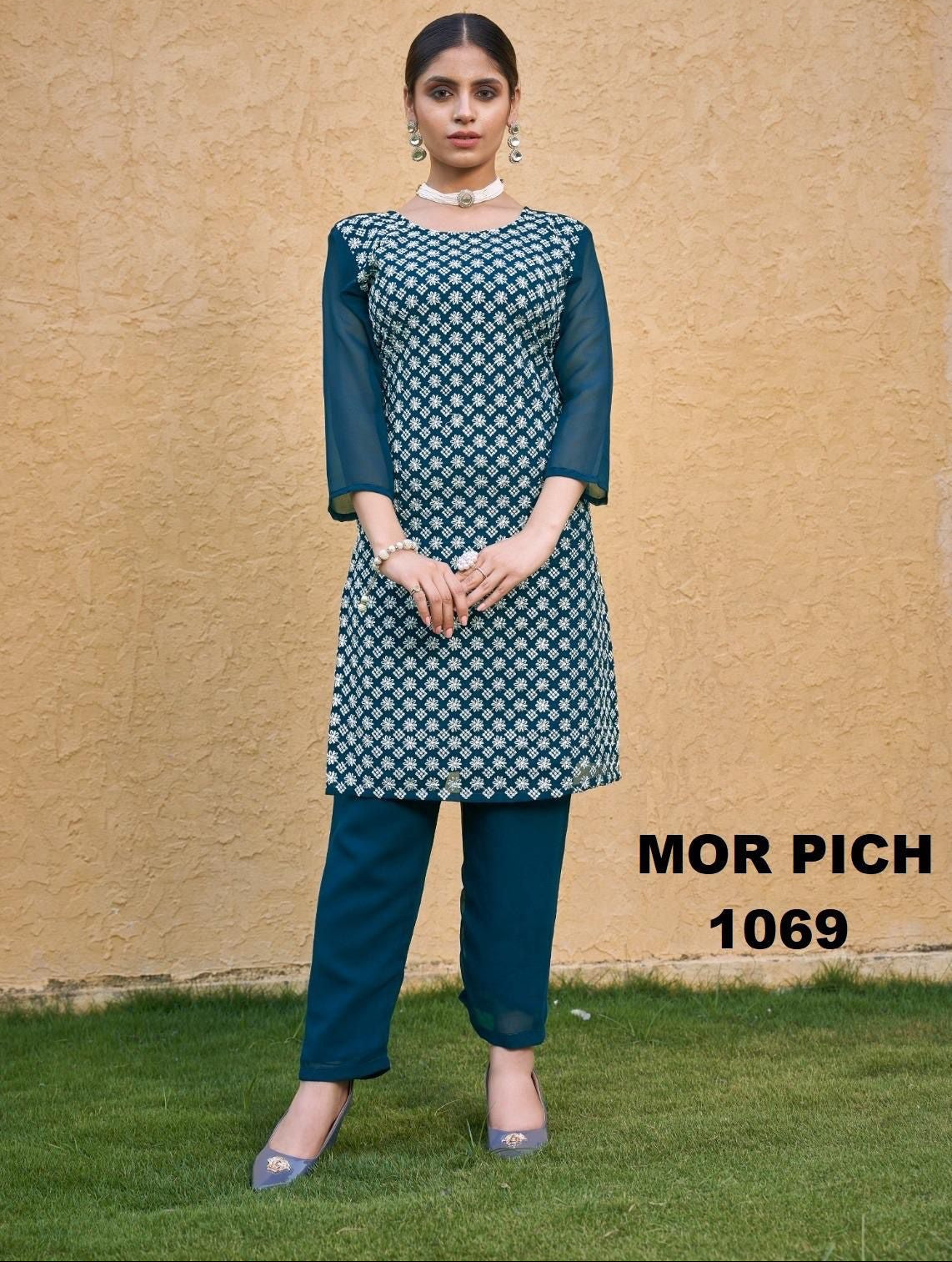 Woman wearing a green and white patterned kurta with blue pants against a beige wall.