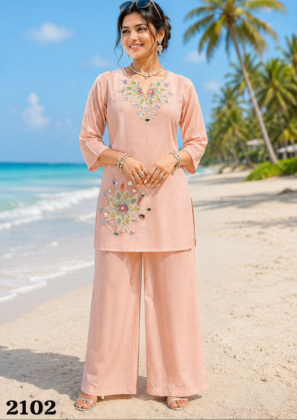 Woman in a pink embroidered outfit standing on a beach with palm trees in the background