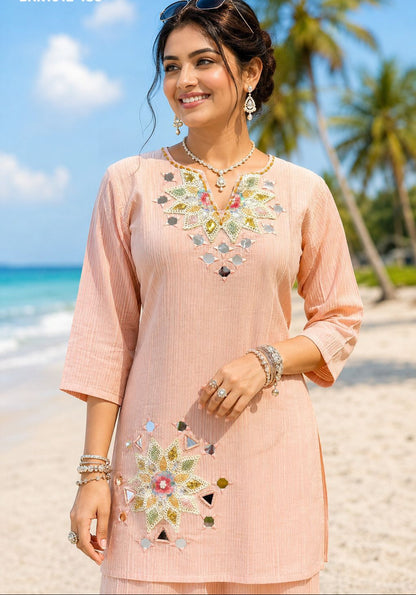 Woman in a peach embroidered dress standing on a beach with palm trees in the background